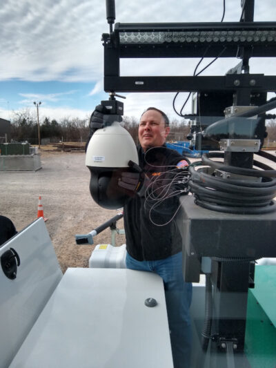A corporate team member handily installs a surveillance camera on one of their new MPS CheckPoint mobile guard shacks.